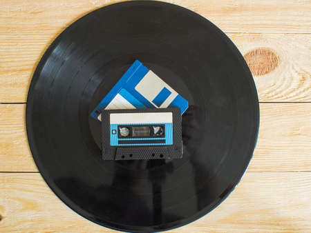 On a wooden background is a vinyl record, and on it are an audio cassette and a floppy disk. Top viewの写真素材