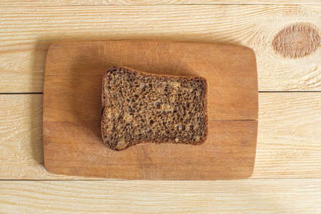 A slice of dark rye bread sits on a small cutting board that sits on a wooden background. Top viewの写真素材