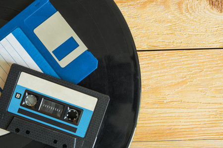 On the vinyl record are an audio cassette and a floppy disk. The record itself lies on a wooden...