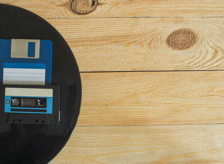 On a wooden background with knots lies an audio cassette, a floppy disk and a vinyl record. Top view. Space for textの写真素材