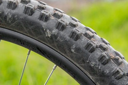 Part of a mountain bike wheel with a studded, slightly dirty tire. On a blurry green background....