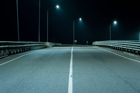 An asphalt road with a solid white line lit by streetlights. Night scenes
