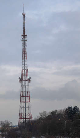 Telecommunication tower with antennas against the background of the cloudy sky and treesの写真素材