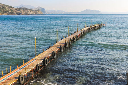A colored wooden pier with car tires goes into the sea. Mountains are visible on the horizon. Calm...