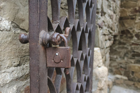 An old rusty metal wrought-iron door with a padlock on the background of a stone wallの写真素材