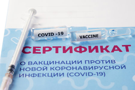 Close-up of the vaccination certificate, a syringe and two ampoules with the vaccine. Translation: certificate of vaccination against a new coronavirus infection COVID-19のeditorial素材