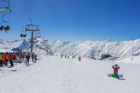 Georgia, Gudauri, March 8, 2013: The cable car and a lot of people under it. Against the background of snow-capped peaks and blue sky. The concept of active winter recreationのeditorial素材
