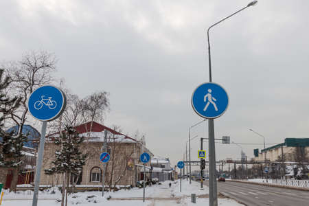 Blue road signs against a gray snowy sky. Snow lies on the sidewalk where the signs are installed. They inform about the bicycle lane and the pedestrian zone. Krasnodar, Russia, February 18, 2021のeditorial素材