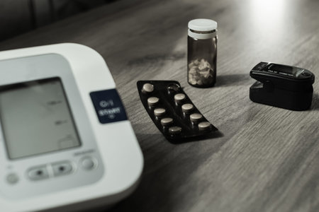 On a wooden table there is an automatic tonometer, tablets and an oxyometer. Black and white photo....