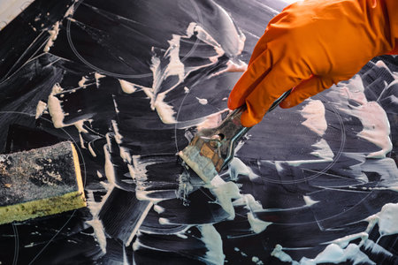 Orange glove, metal scraper, sponge and foam cleaner. Washing the cooktop. Selective Focus. The...