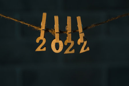Wooden numbers 2022 are suspended from a string with wooden clothespins. Dark background. Happy new year and christmasの写真素材