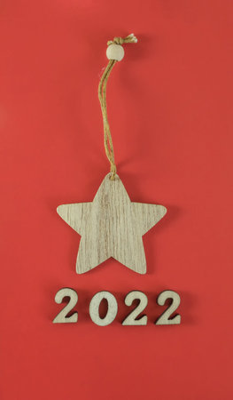 Wooden toy star and wooden numbers 2022 on a red background. Environmentally friendly new year 2022....