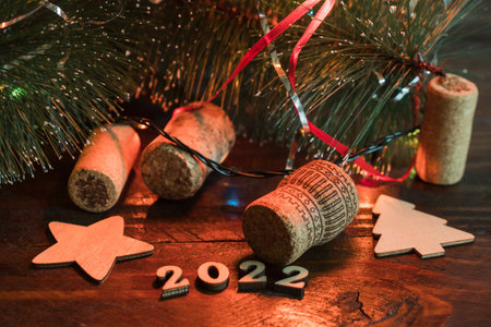 Happy New Year 2022. On a wooden background under the Christmas tree are the symbols of the new year, a Christmas tree, a snowflake, champagne corks and the numbers 2022の写真素材