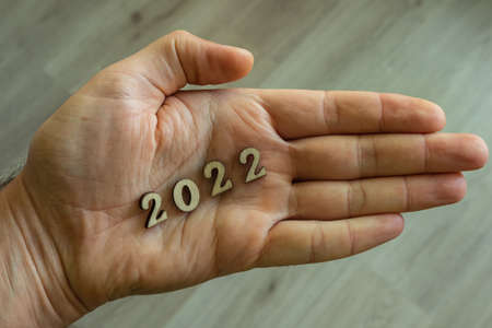 On the palm of a man's hand are the wooden numbers 2022. Minimalism and ecology as a way of lifeの写真素材