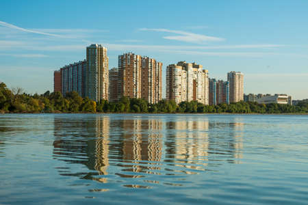 Multistory buildings on the river bank. In the background is a blue sky with beautiful clouds. The buildings are reflected in the water. Cityscapeの写真素材