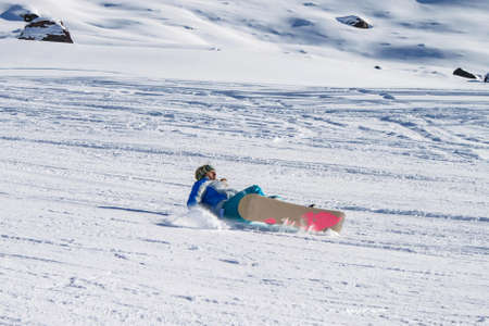 A girl snowboarder falling on her back on a ski slope. Getting injured in winter sports. Active winter recreationの写真素材