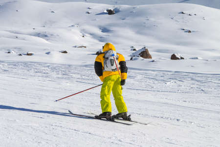 A bright yellow skier is riding backwards on a ski slope. In the background snowy mountains. Active winter holidaysの写真素材