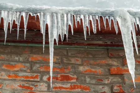Icicles on the roof of the house against a red brick wall. Droplets of water fly down from the icicles. Winter sunny day in the countrysideの写真素材