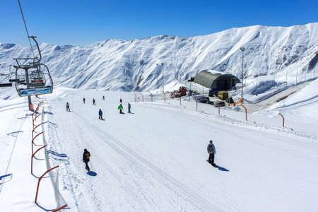 View from the cable car to the ski slope with snowboarders. In the background is a snowy mountain range and a clear blue sky. Active winter holidays in the mountainsの写真素材