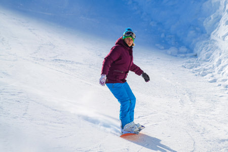 A young pretty girl slides down the slope on a snowboard. Lone snowboarder on the ski slope. Active recreation during the winter vacationsの写真素材