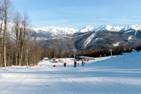 Gentle ski slope against the backdrop of a chairlift, snowy mountains and blue skies. Winter sports...