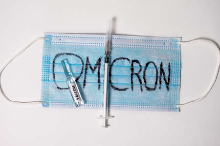 A blue medical mask with Omicron written on it, a syringe and an ampoule of vaccine on a white background. Protection against a new kind of coronavirus covid 19. Top viewの写真素材