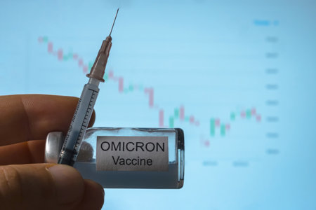In his hand is a syringe and an ampoule with a vaccine against Omicron, a new type of coronavirus Covid-19. Against the background of a falling stock market chart. Close-upの写真素材