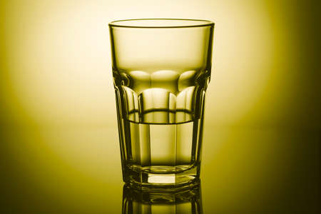 Half-filled highball glass in yellow light with mirror reflection. Close-upの写真素材