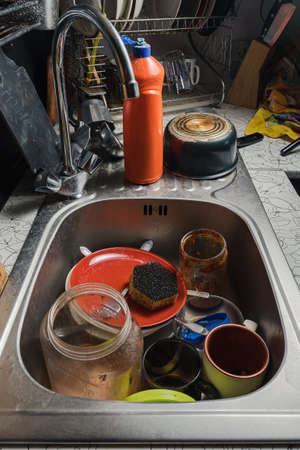 A sink with dirty dishes. There is detergent, plates and glasses in the background. Home kitchen with dirty dishesの写真素材