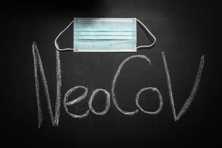 NeoCov inscription made in chalk on black board. Next to it hangs a blue medical mask. NeoCov is a strain of the Covid-19 coronovirus discovered in Africa in 2022の写真素材