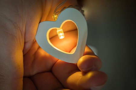 A man's hand holds a glowing yellow heart. Valentine's day concept. February 14 is the Day of All...