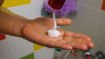 A close-up of white hair conditioner pouring out of a tube onto a woman's palm. In the background, a colorful tile. The concept of health and body careの写真素材