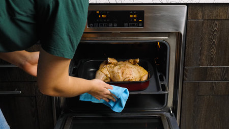 Close-up of a woman's hand sending a whole raw chicken rubbed with spices into the oven for baking