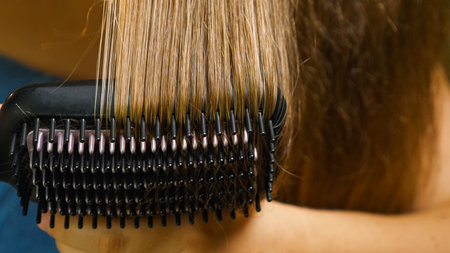 Close-up of a woman brushing and drying her hair with an electric hair straightener. Heated, ceramic, non-damaging hair brushの写真素材