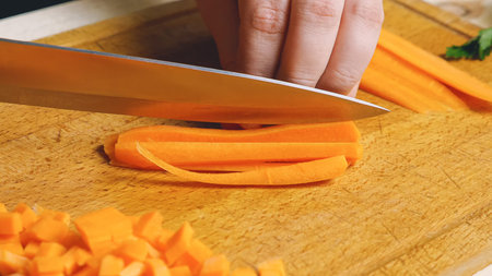 Cutting carrots on a cutting board into straws and then cubes. Healthy and wholesome food every day....