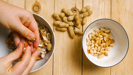 Top view of women's fingers peeling peanuts from their shells. A handful of peanuts lying on a...