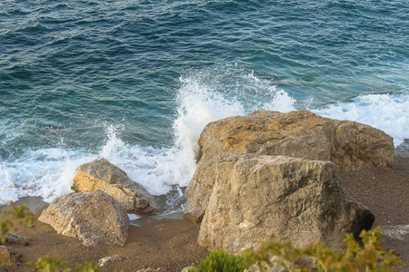 Seascape. Large boulders of stone lie on the sandy beach. The wave of the black sea hits the rocks...