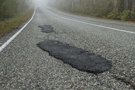Fresh patches after patching the road. Country highway in the foggy forest. bad road conditionの写真素材