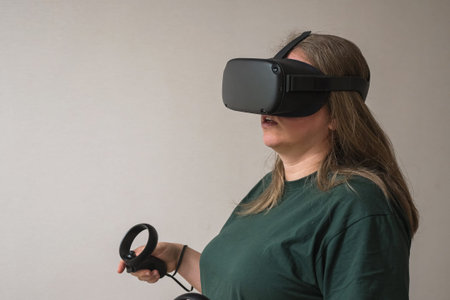 A girl in a virtual reality helmet wearing a green T-shirt stands against a gray wall. The woman...