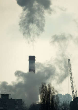 Smoke and steam from the CHP chimney. Nearby, a crane is working. In the background, gray smog-covered sky. environmental problems. The global energy crisisの写真素材