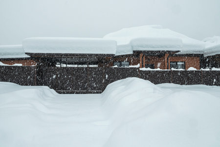 A private brick house and street covered with snow. There is a thick layer of snow on the roof of the house. It is snowing heavily. The snowy winter in Europe. The global problems of climate changeの写真素材