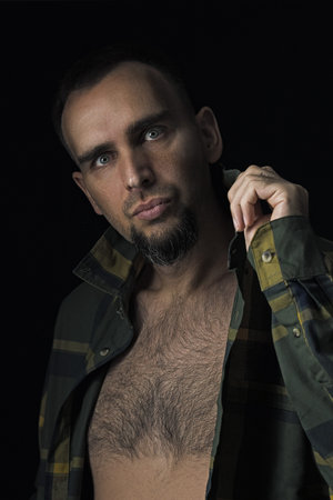 Portrait of a sexy, handsome man looking into the camera. Guy with a beard in an unbuttoned checked...