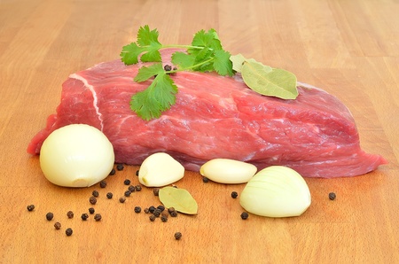 A piece of raw beef with onion and spices on a wooden tableの写真素材