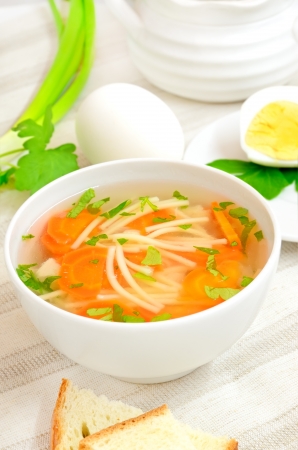 Soup with pasta and vegetables in white bowl on a tableの写真素材