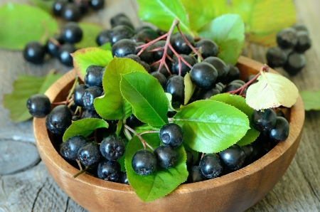Black chokeberry in brown bowl on wooden tableの写真素材