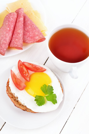 Breakfast - sandwich with fried egg, tomato slices and tea on wooden tableの写真素材