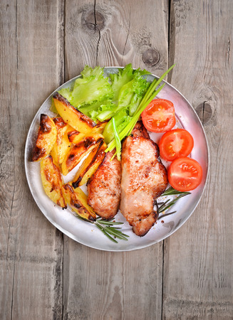Pork steaks, baked potato wedges and fresh vegetables on rustic table, top viewの写真素材