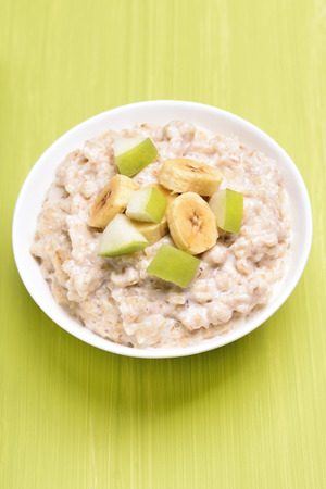 Oatmeal porridge with fruit slices in white bowl, top viewの写真素材