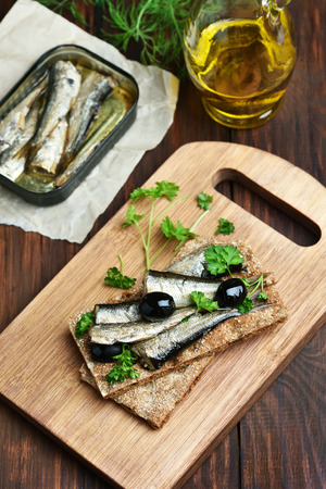 Crispbread with sprats and olives on wooden cutting boardの写真素材
