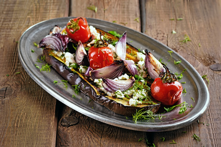 Roasted eggplant with tomatoes, onion and herbs on wooden tableの写真素材